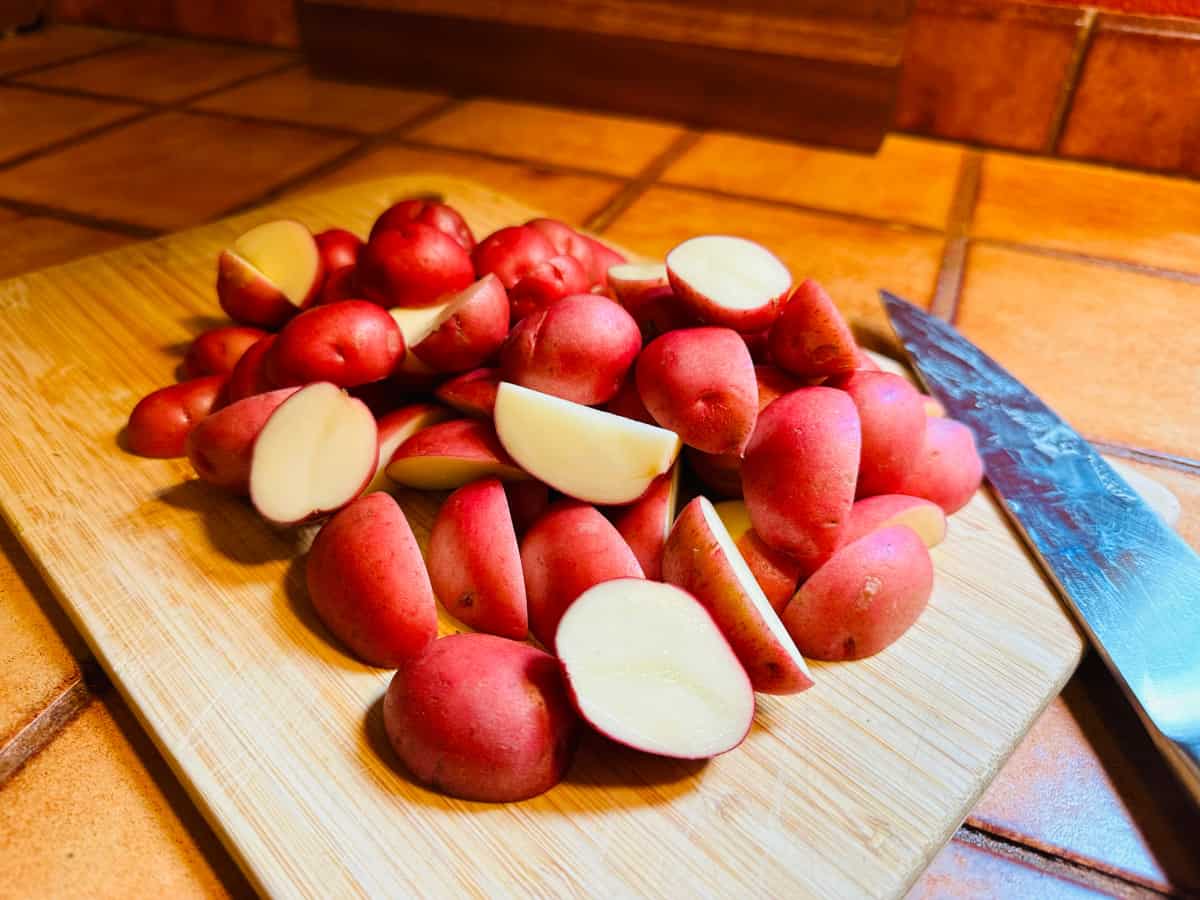 Pieces of small red potato on a cutting board with a chef's knife.