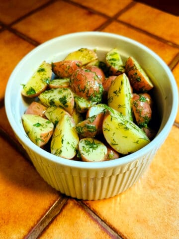 Dill potatoes in a round white ceramic dish with vertical ridges around the sides.