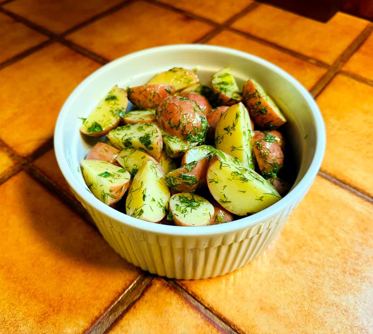 Dill potatoes in a round white ceramic dish with vertical ridges around the sides.