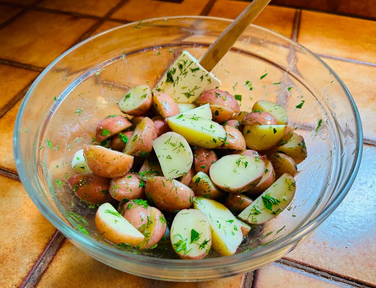 Dill potatoes in a glass bowl with a white silicone spatula.