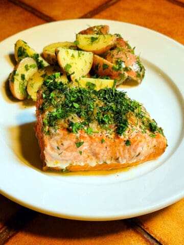 Herbed salmon on a white plate with herb flecked red potatoes behind.
