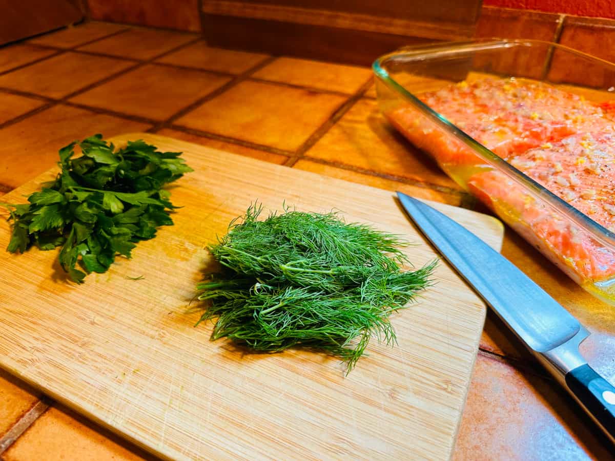 Fresh dill and parsley sprigs on a cutting board next to a chef's knife.