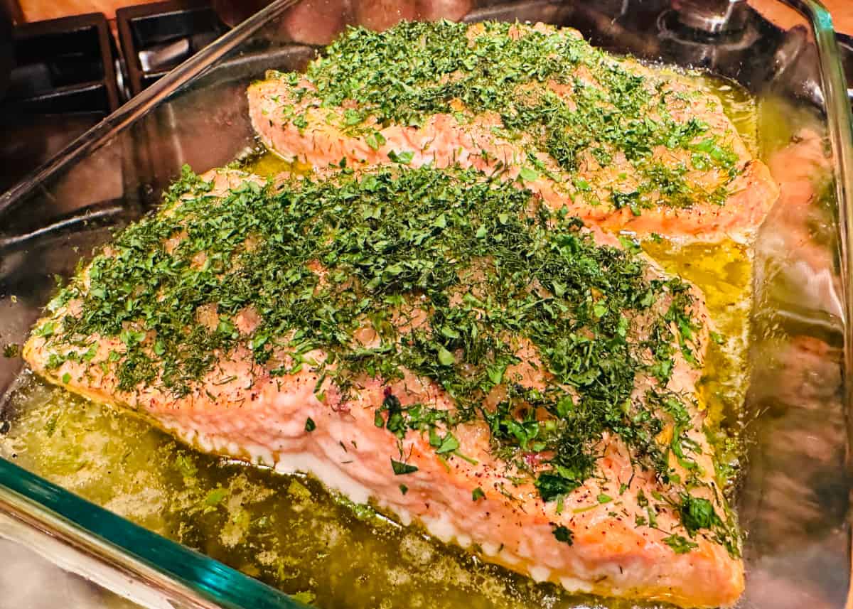 Roasted herbed salmon resting in a glass roasting dish on the stove.