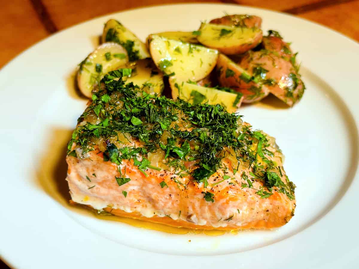 Herbed salmon on a white plate with herb flecked red potatoes behind.