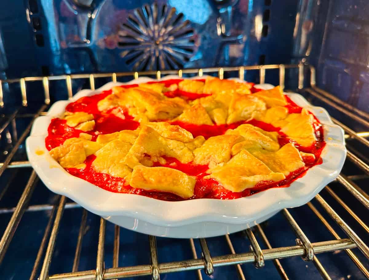 Strawberry pandowdy in a white ceramic pie plate baking in a blue oven.
