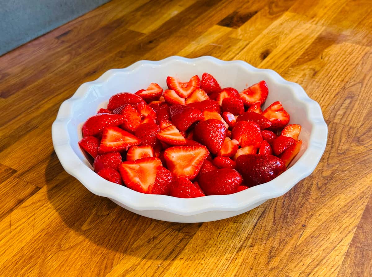 Sliced strawberries in a white ceramic pie plate.
