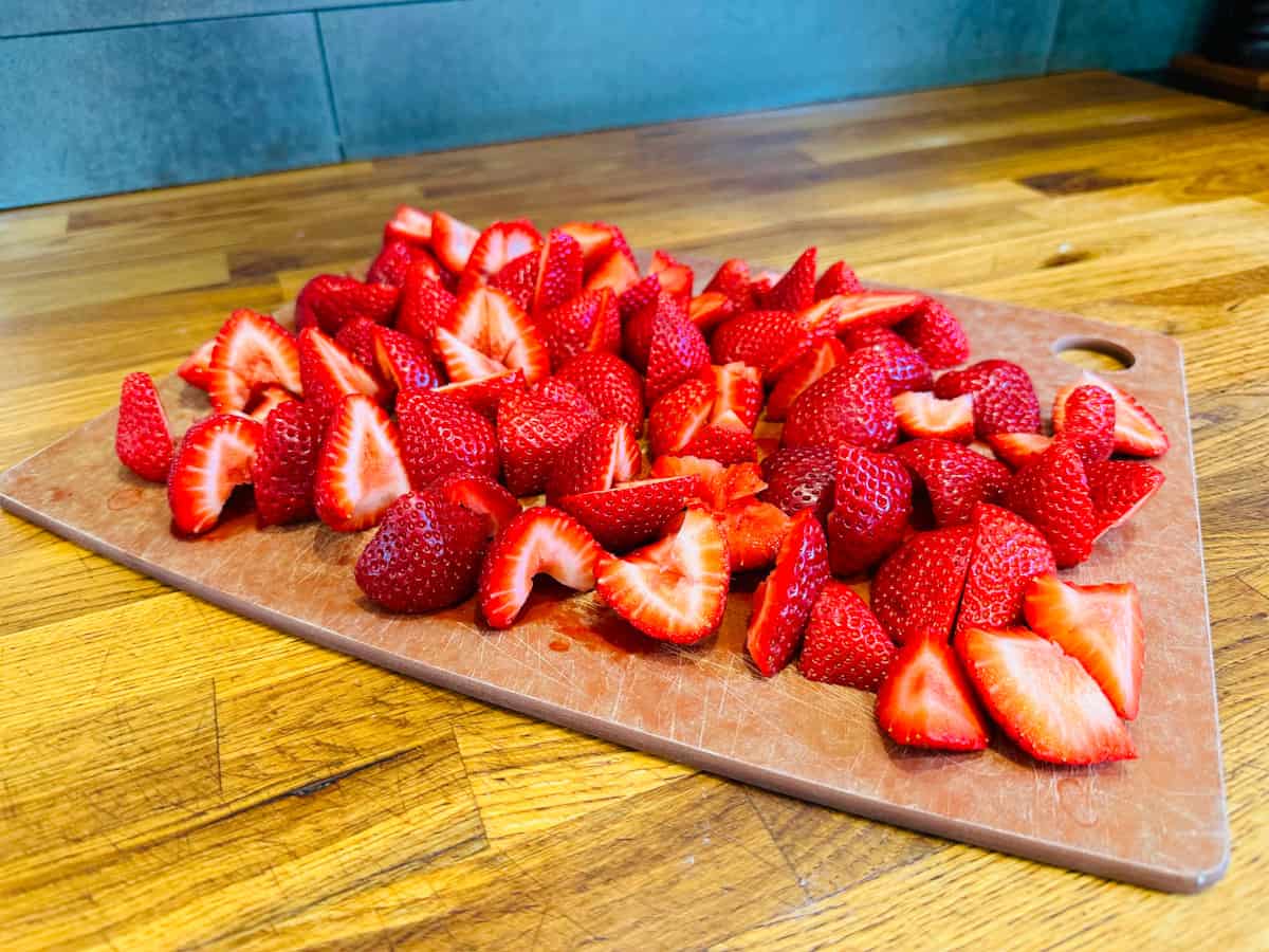 Sliced strawberries on a wooden cutting board.