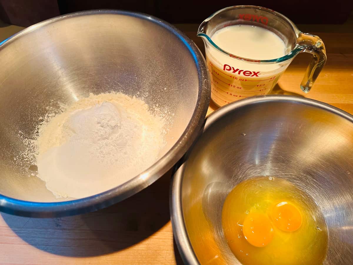 Dry and wet ingredients in separate steel bowls with measuring cup full of buttermilk.