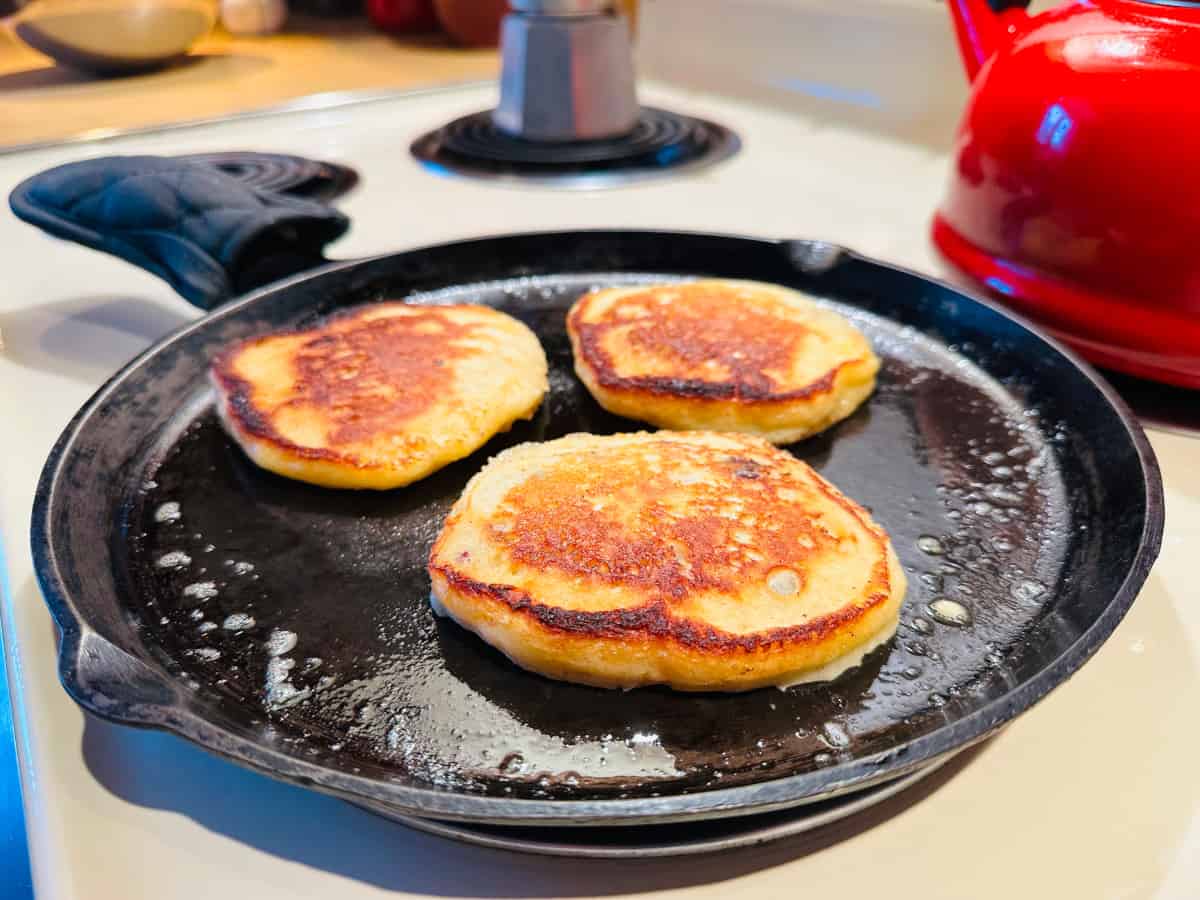 Golden pancakes cooking on cast iron griddle.
