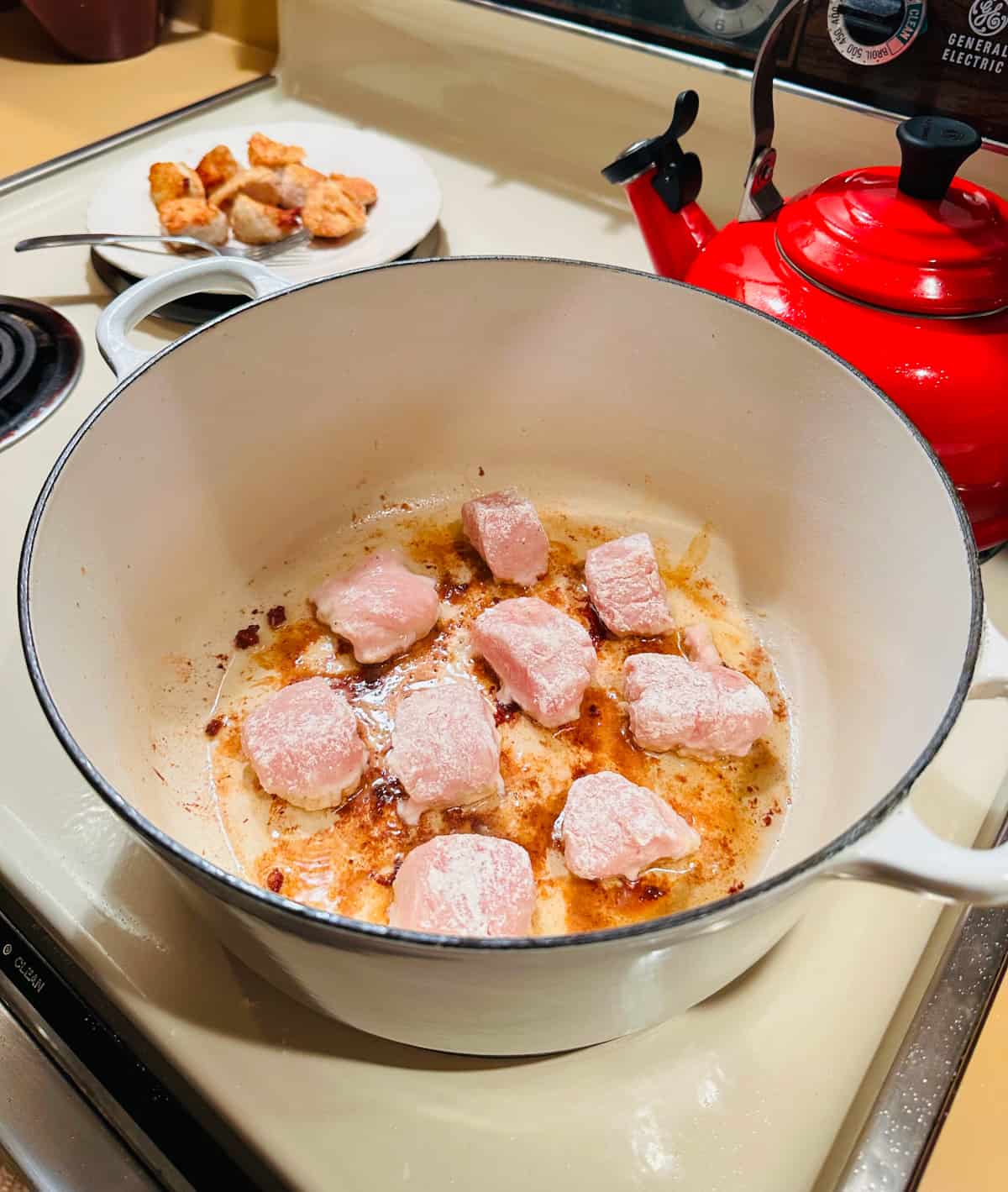 Chunks of chicken frying in a white pot.