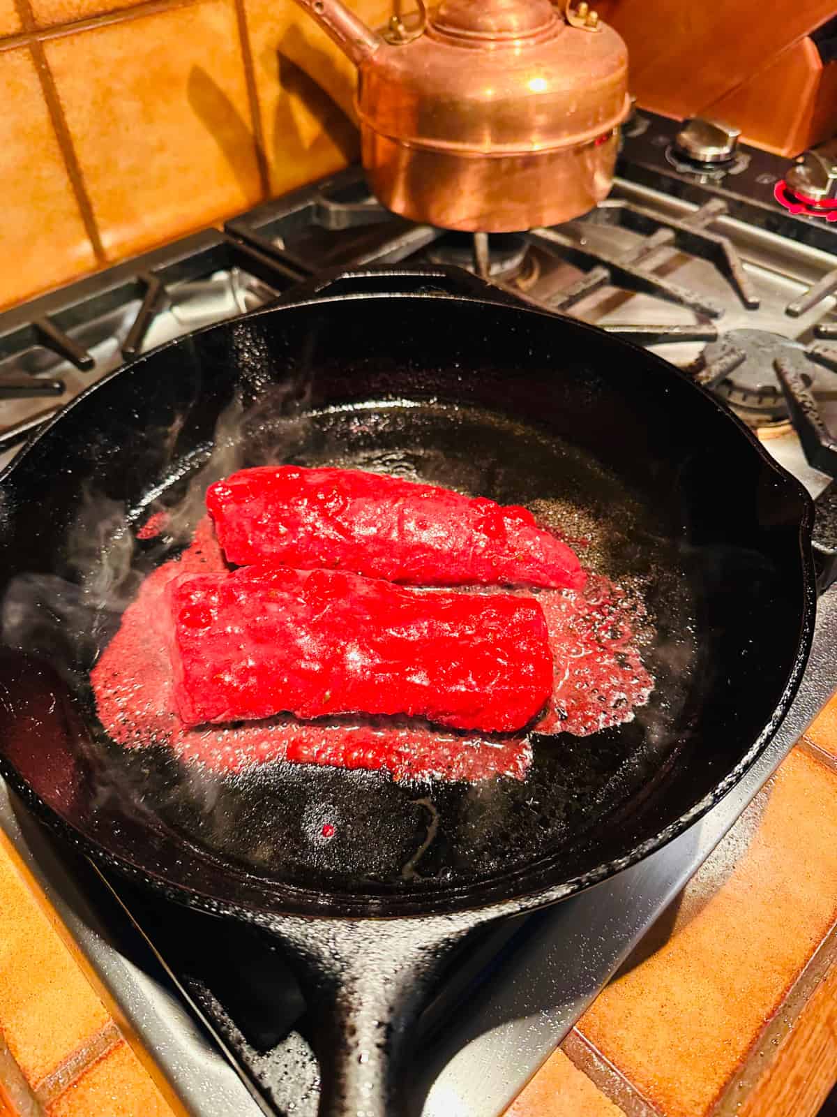 Marinated pork tenderloin frying in a black skillet.