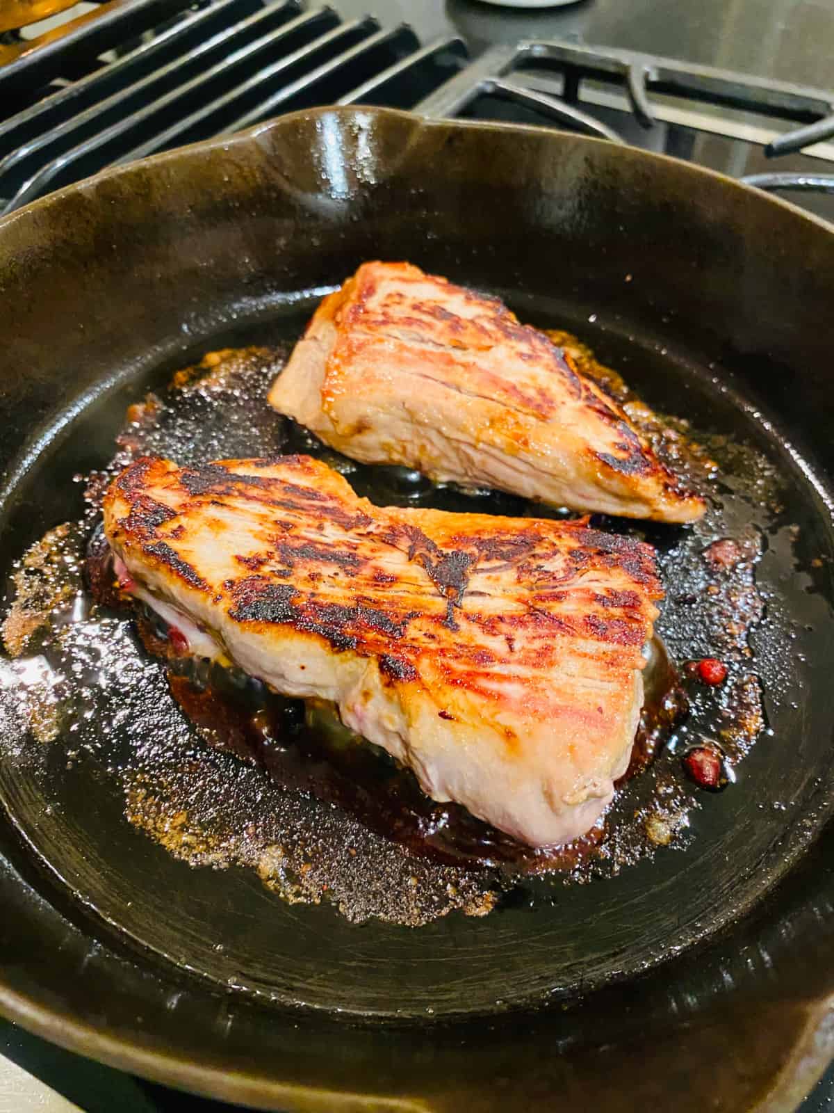 Marinated pork tenderloin frying in a black skillet.