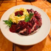 Pork tenderloin with lingonberry gravy and mashed potatoes on white plate.