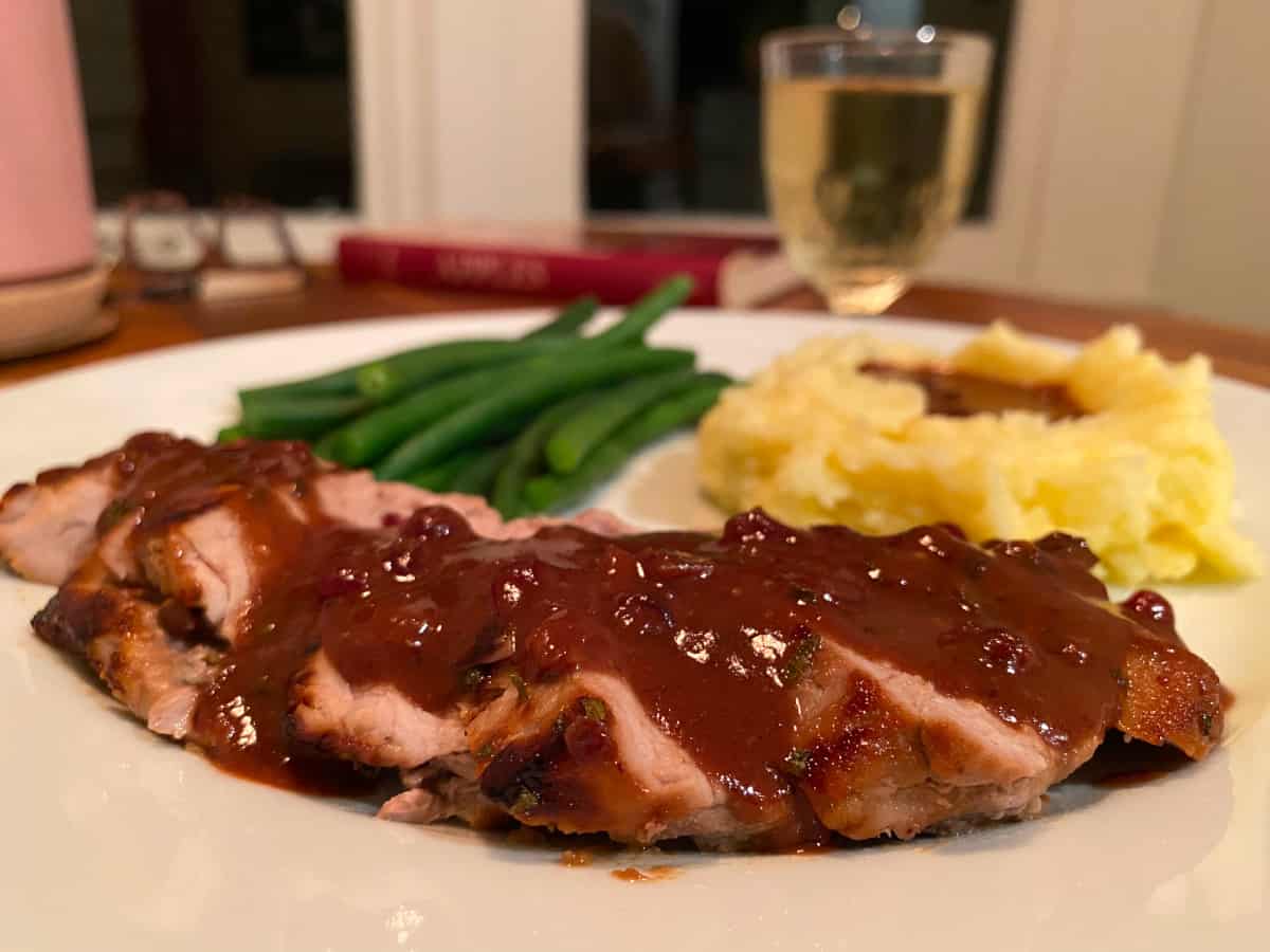 Pork tenderloin with lingonberry gravy, mashed potatoes, and green beans on a white plate.