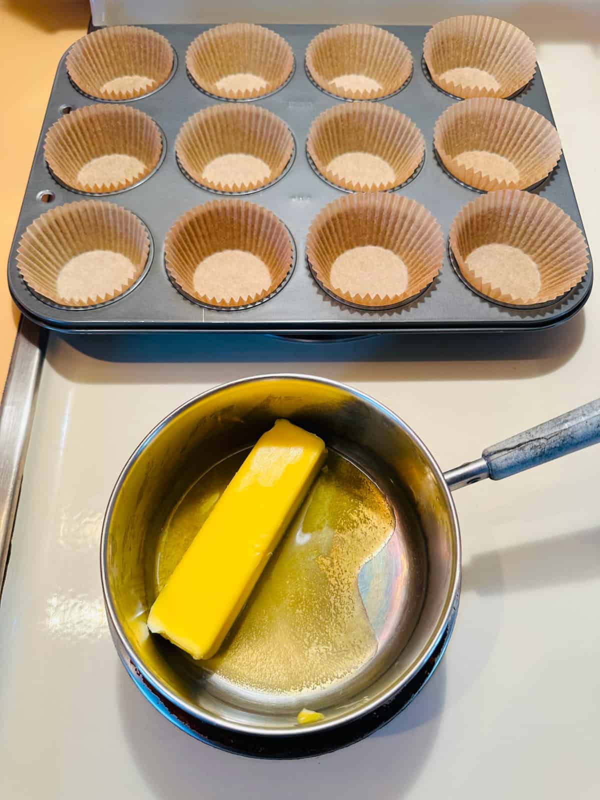 Butter melting in small pot on stove and muffin tin behind it.