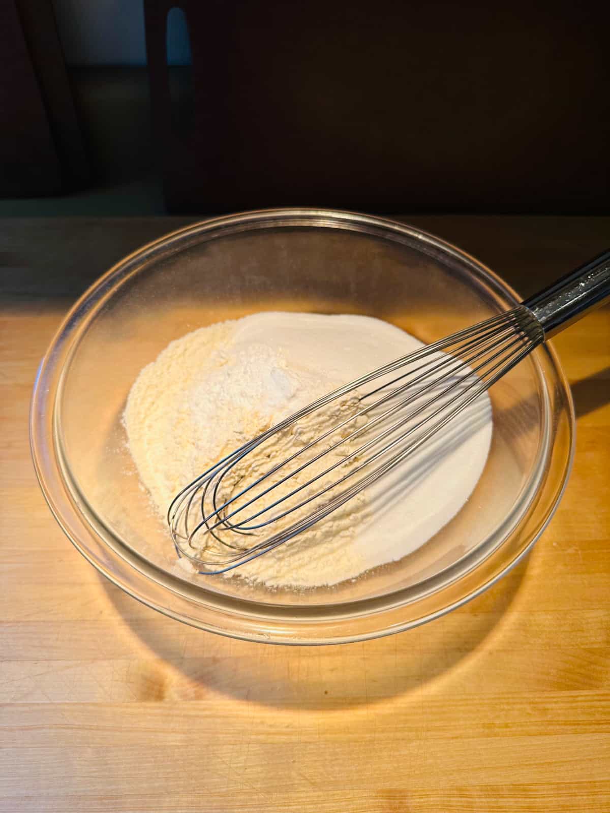 Glass bowl containing dry ingredients and whisk.