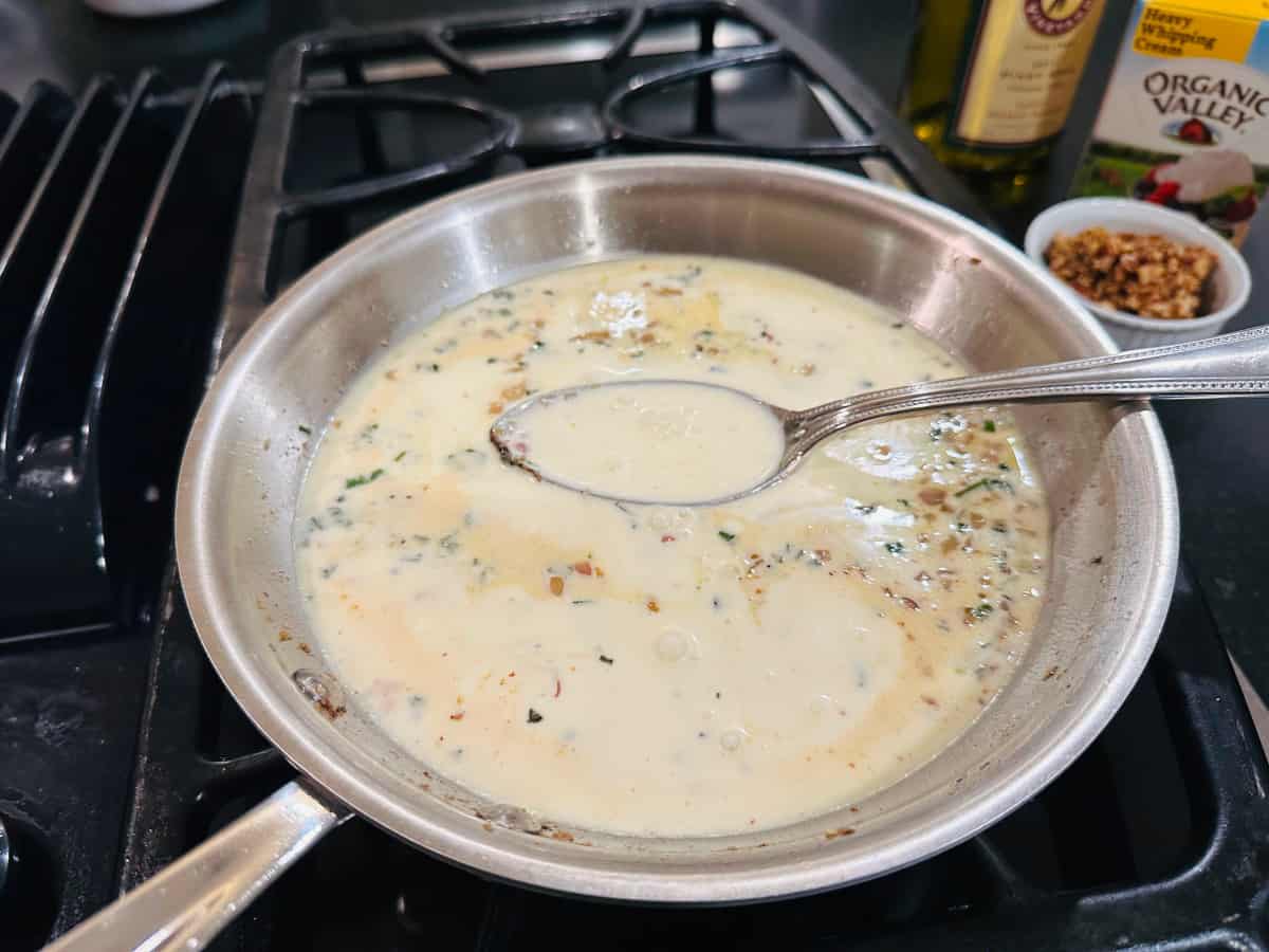 Cream sauce in a steel frying pan with a large spoon.