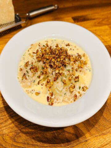 Butternut squash ravioli in a white bowl next to a chunk of parmesan.