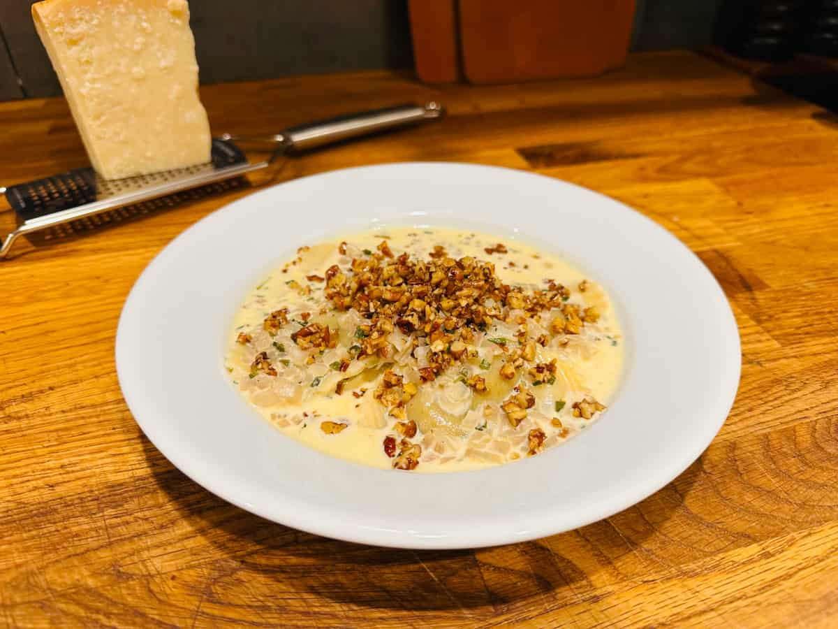 Butternut squash ravioli in a white bowl next to a chunk of parmesan.