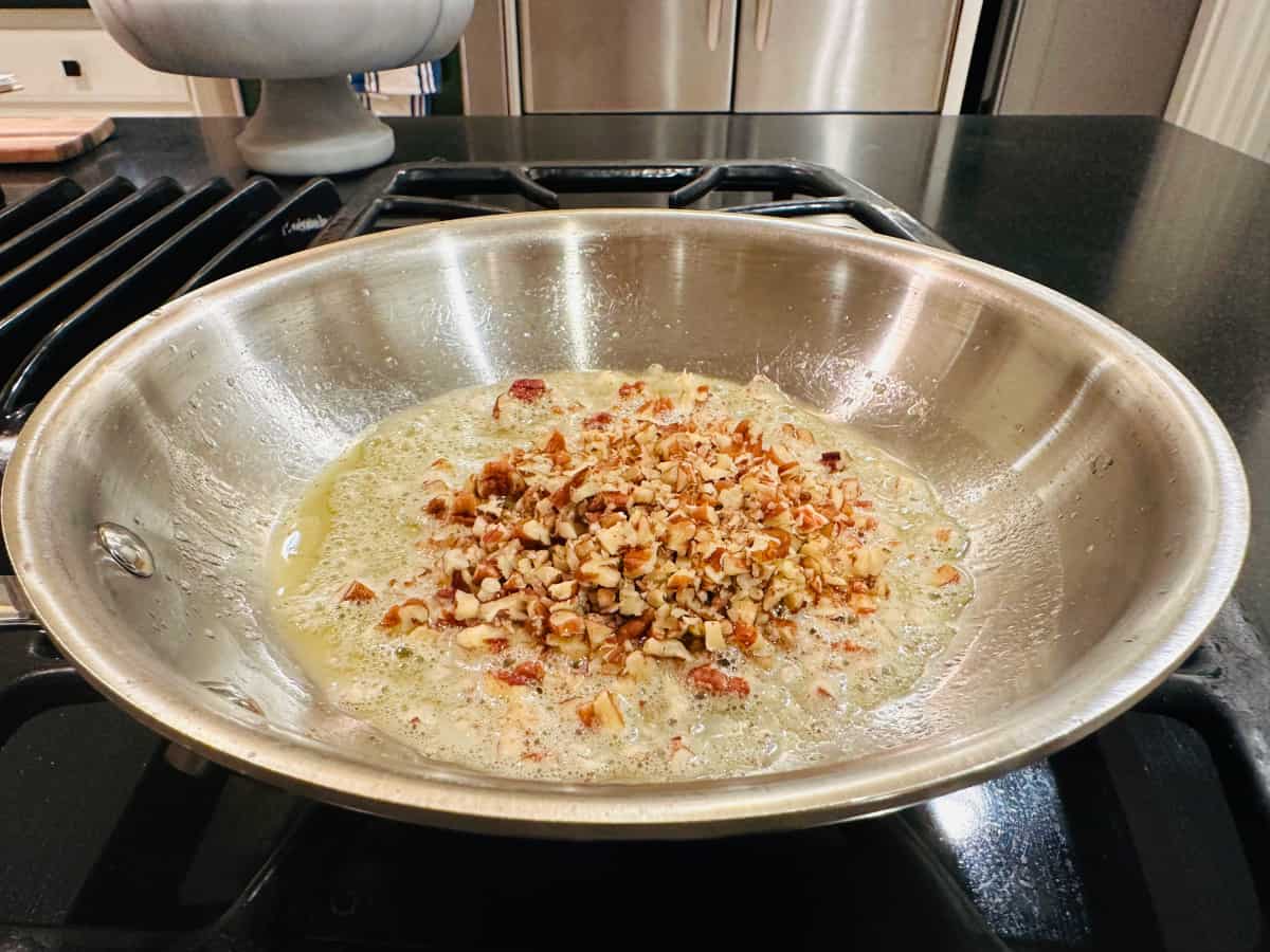 Chopped pecans and melted butter in a steel frying pan.