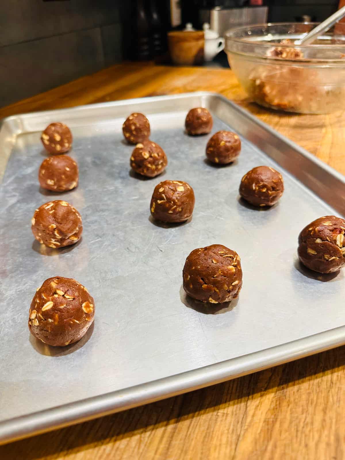 Spheres of chocolate oatmeal cookie dough on metal baking sheet.