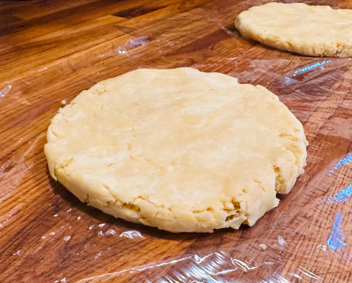 Two disks of finished butter pie dough sitting on plastic wrap.
