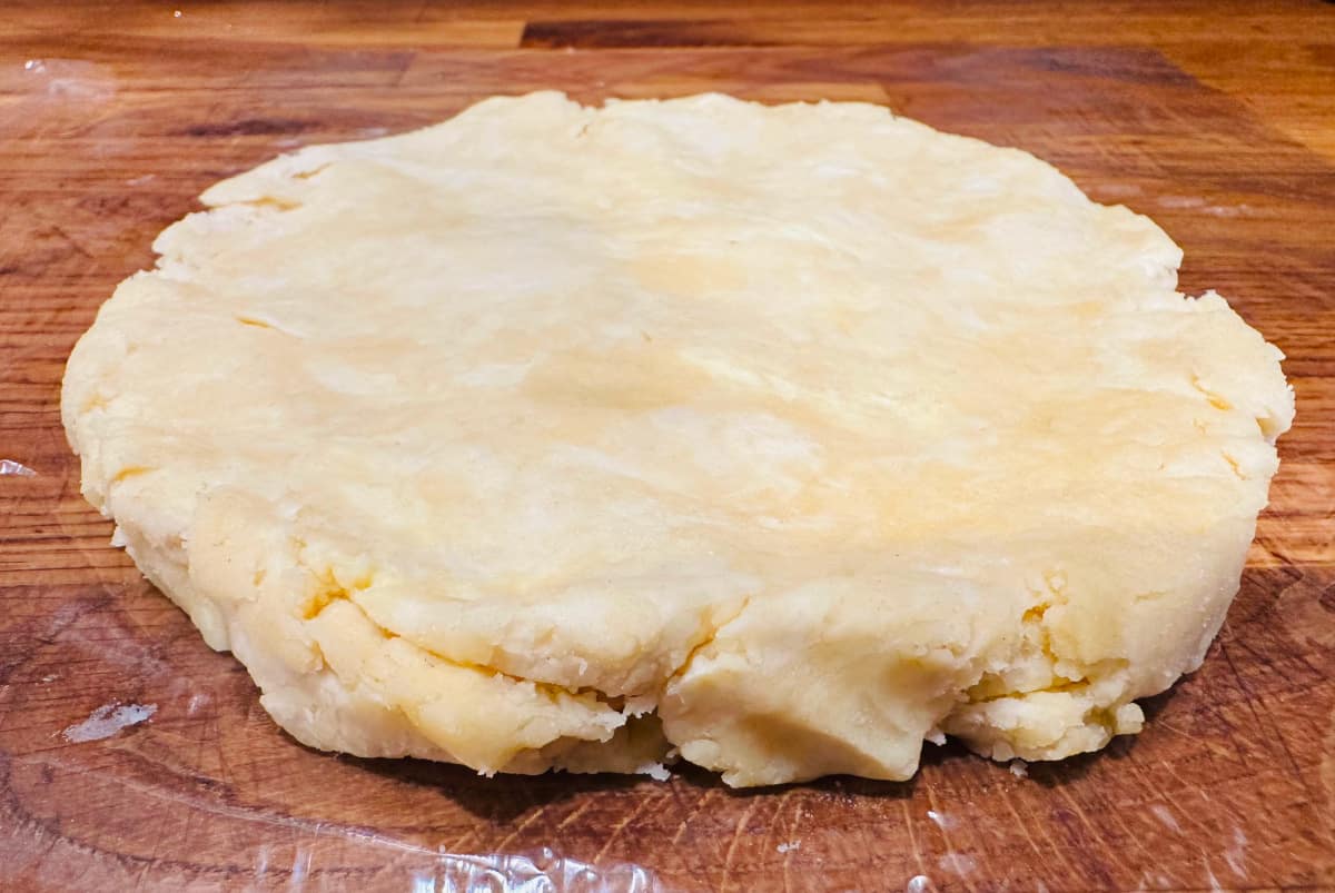 Disk of butter pie dough on plastic wrap.