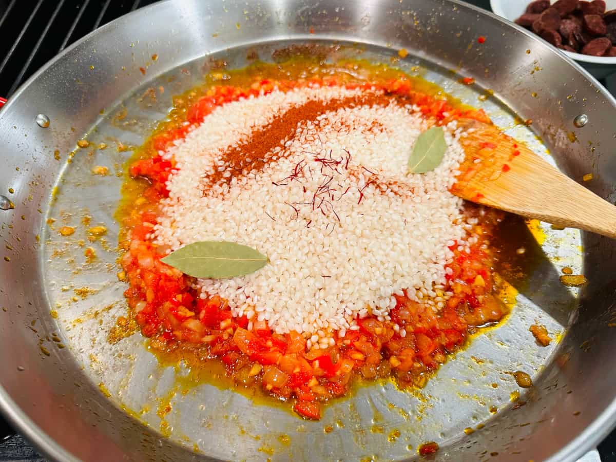 Rice and spices on top of sofrito in a metal pan.