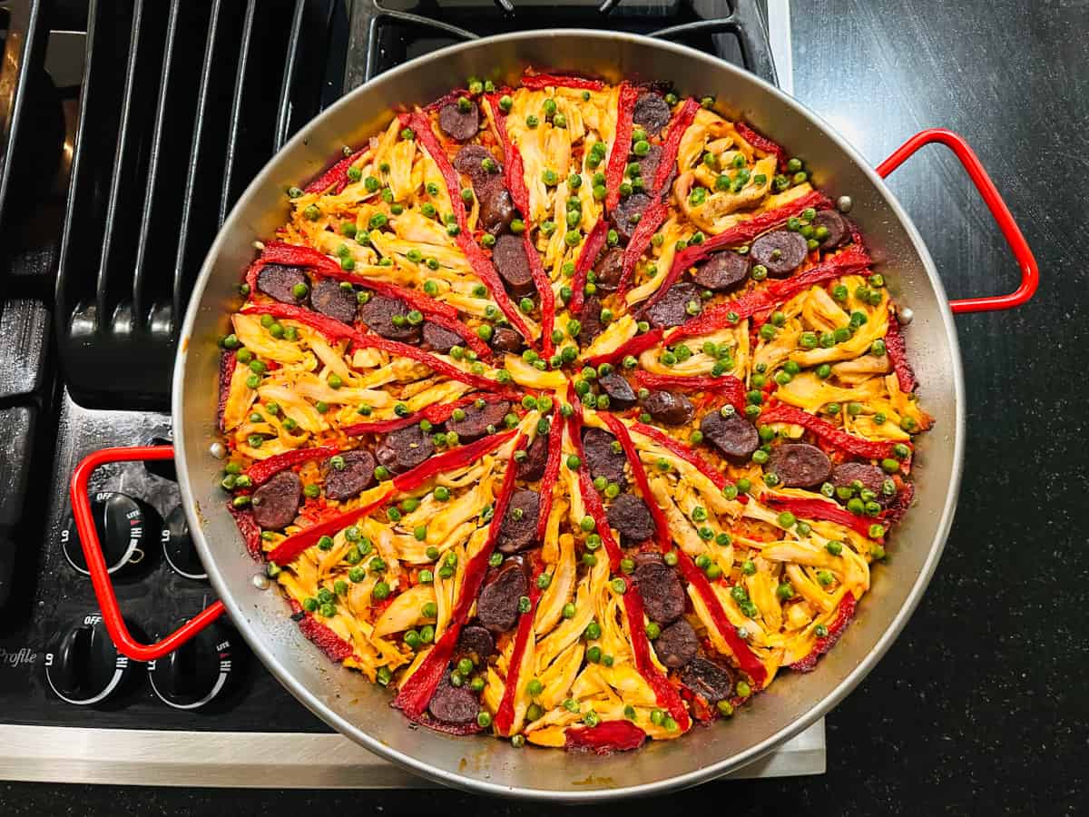 Finished chicken paella in a metal pan with red handles.
