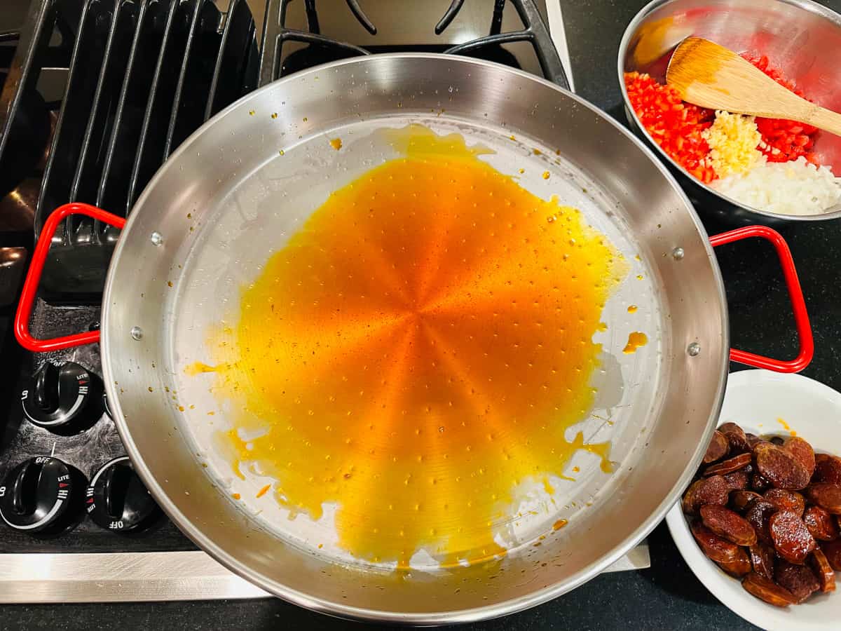 Paella pan containing orange tinted cooking oil.