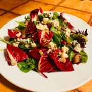 Treviso and baby lettuce topped with blue cheese crumbles and chopped walnuts on a white plate.