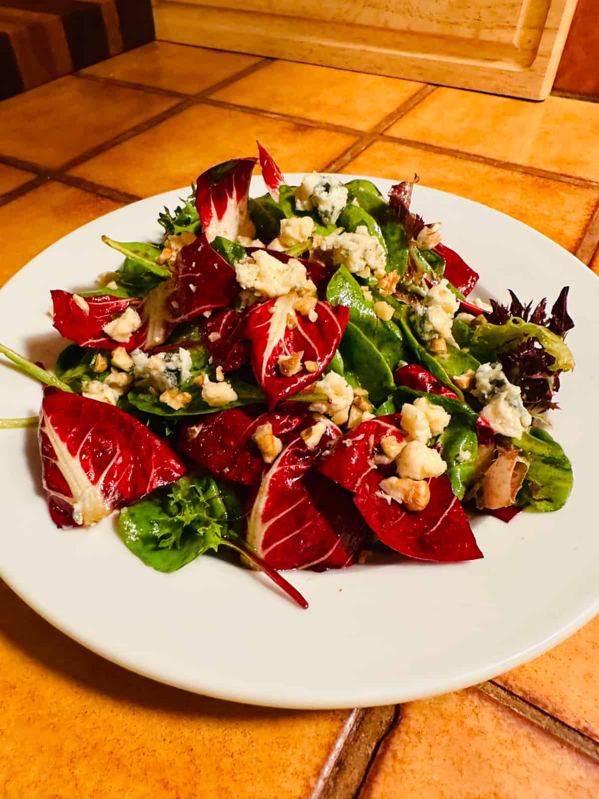 Treviso and baby lettuce topped with blue cheese crumbles and chopped walnuts on a white plate.