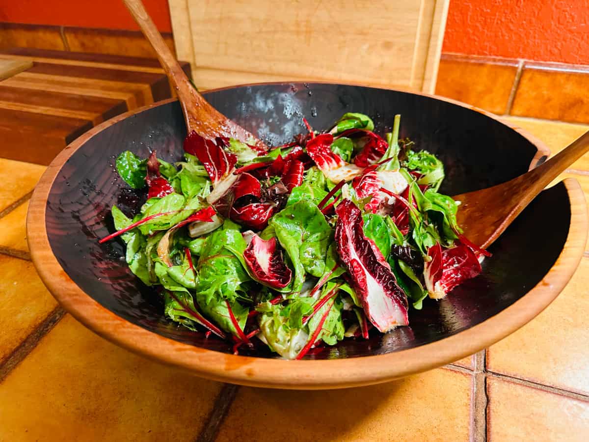 Treviso and baby lettuce in wooden bowl with salad tongs.