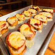 Cooked fontina & prosciutto toasts on a metal baking sheet.