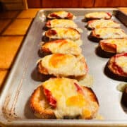 Cooked fontina & prosciutto toasts on a metal baking sheet.