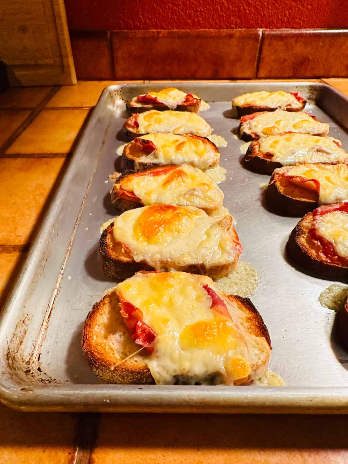 Cooked fontina & prosciutto toasts on a metal baking sheet.