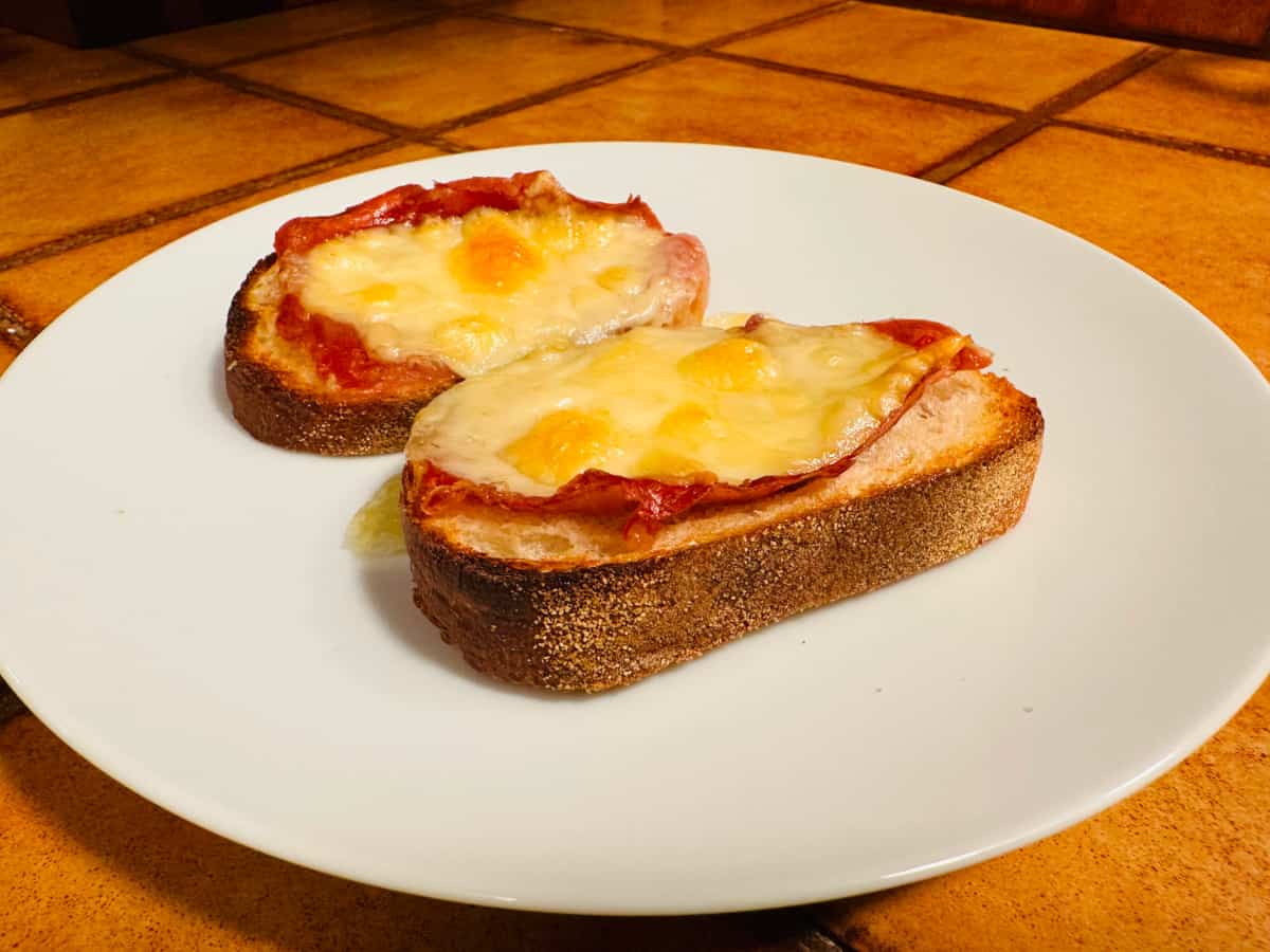 Two fontina & prosciutto toasts on a white plate.