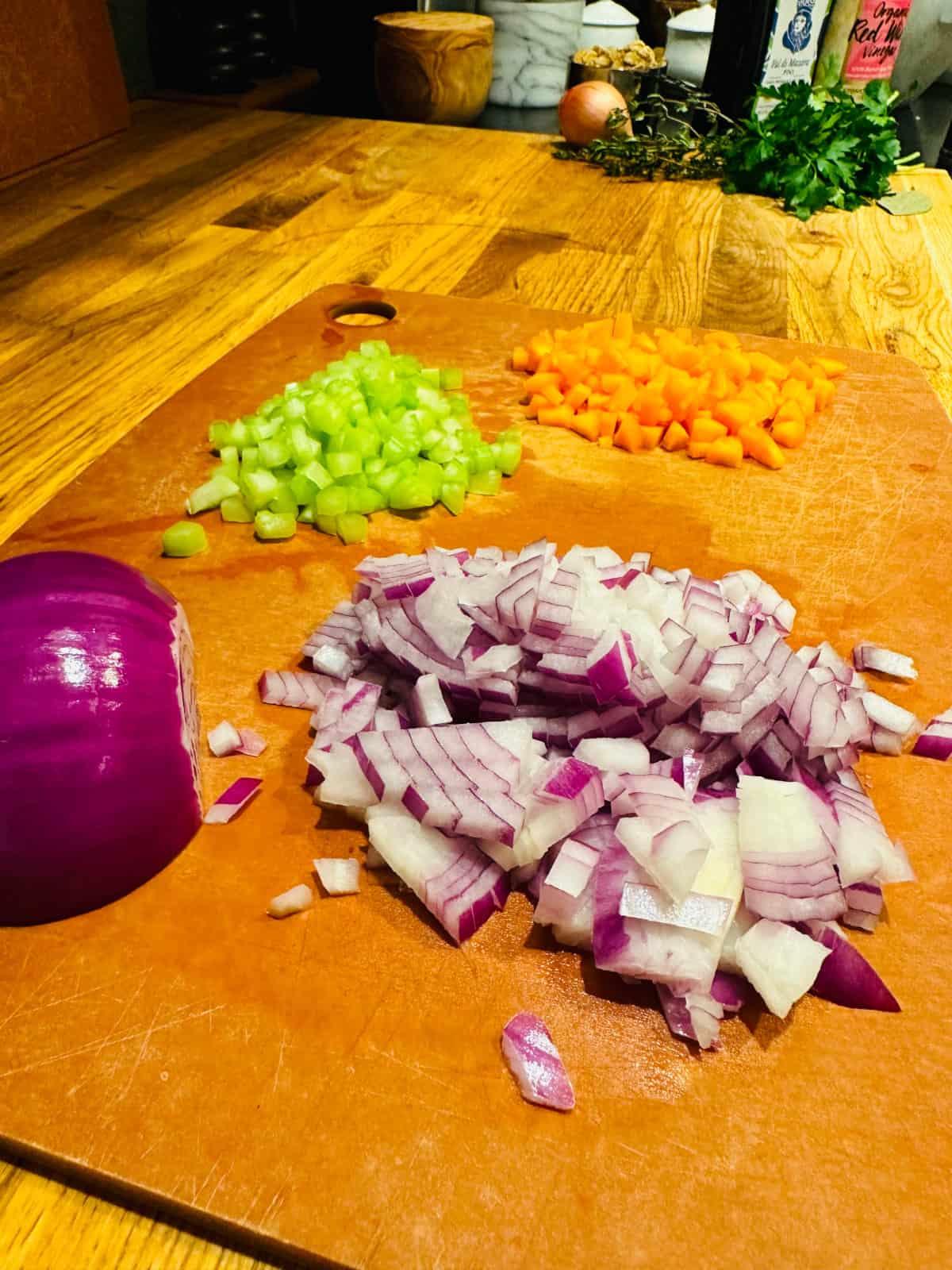 Chopped red onion, celery, and carrot on a wood cutting board.