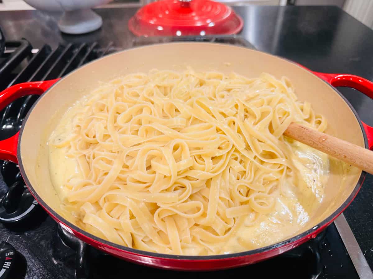 Stirring long noodles into cream sauce with a wooden spoon.