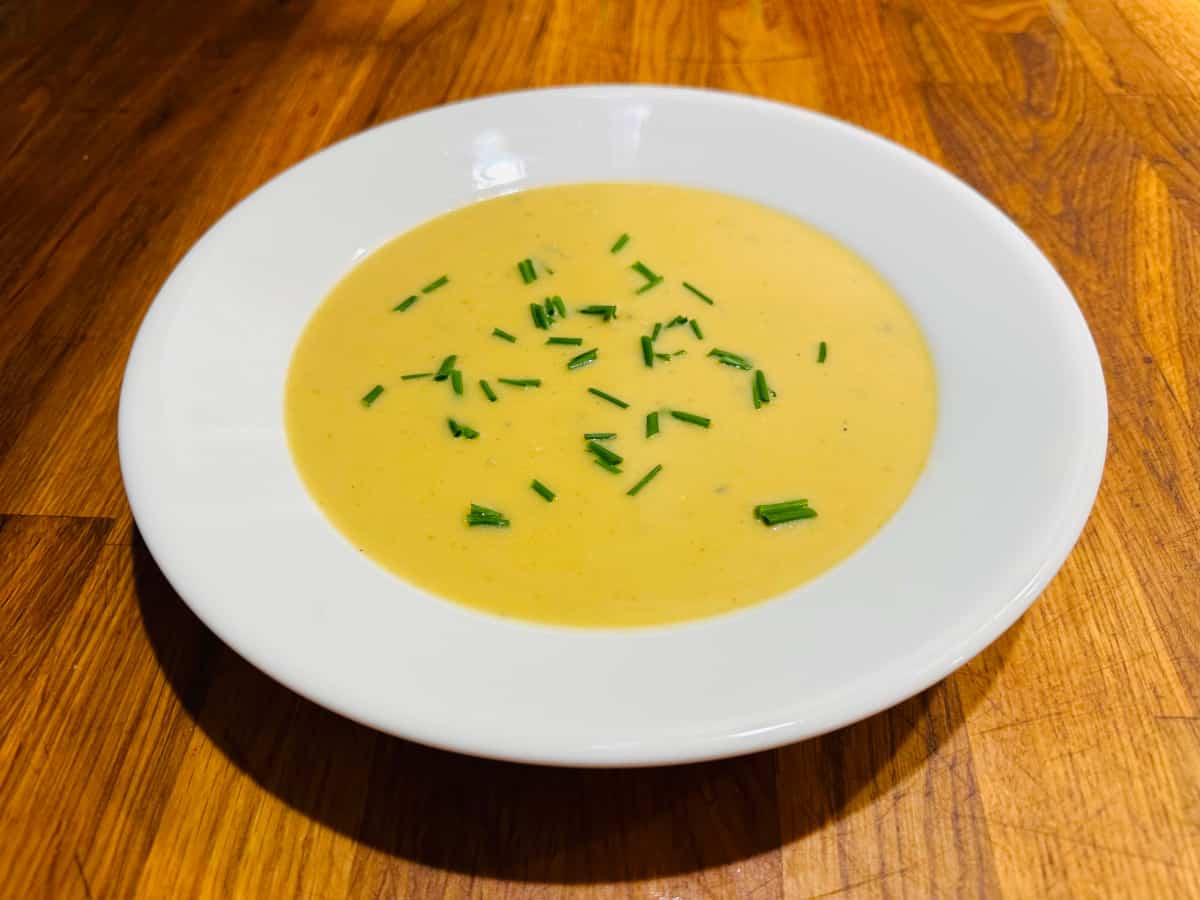 Leek and potato soup with chives on top in a white bowl.