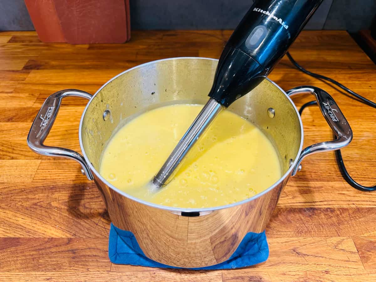 Steel pot containing leek and potato soup and immersion blender.