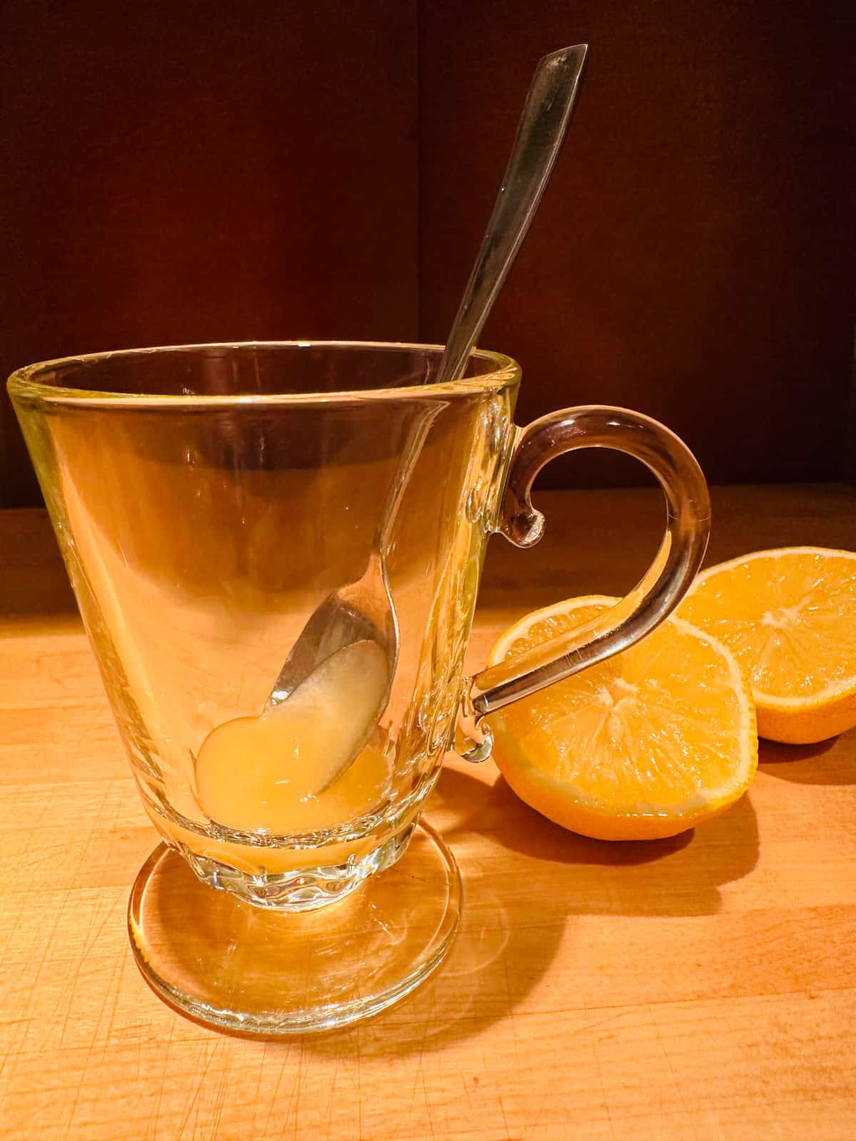 Glass mug with spoon of honey next to two halves of a lemon.