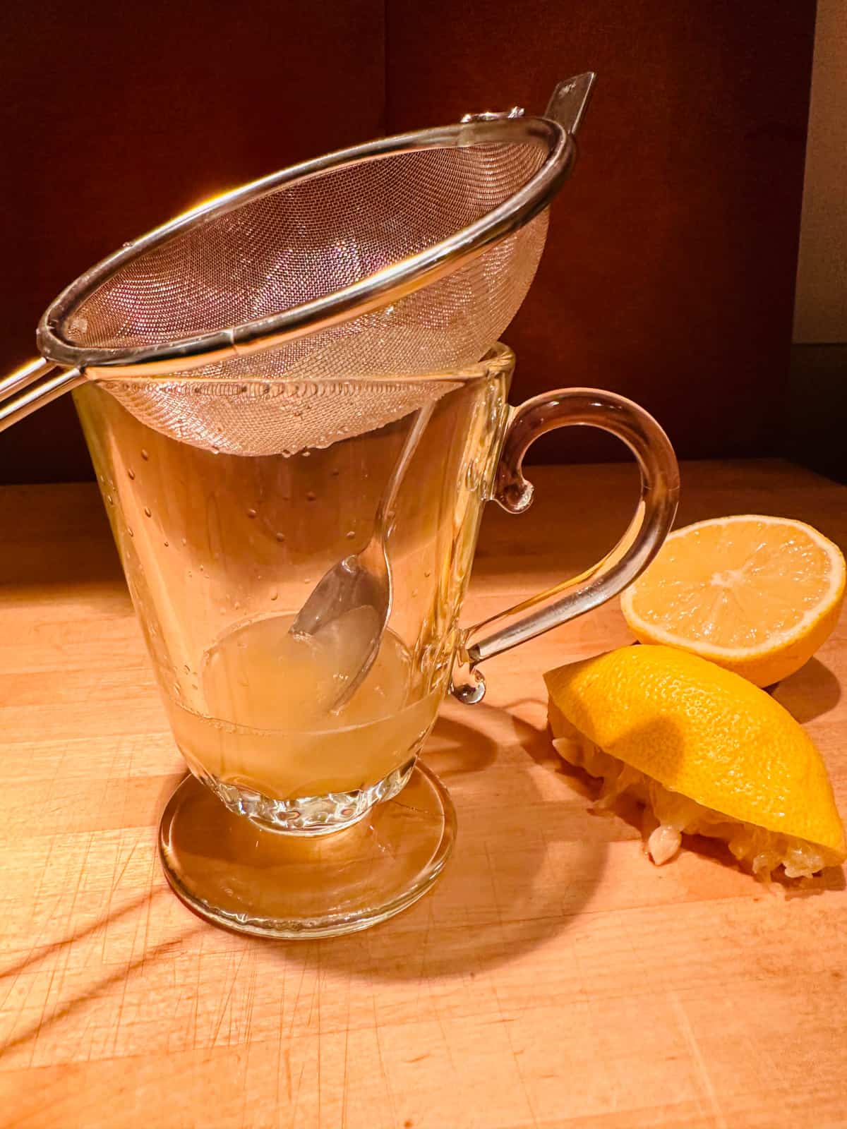 Metal strainer over glass mug containing honey and lemon juice.