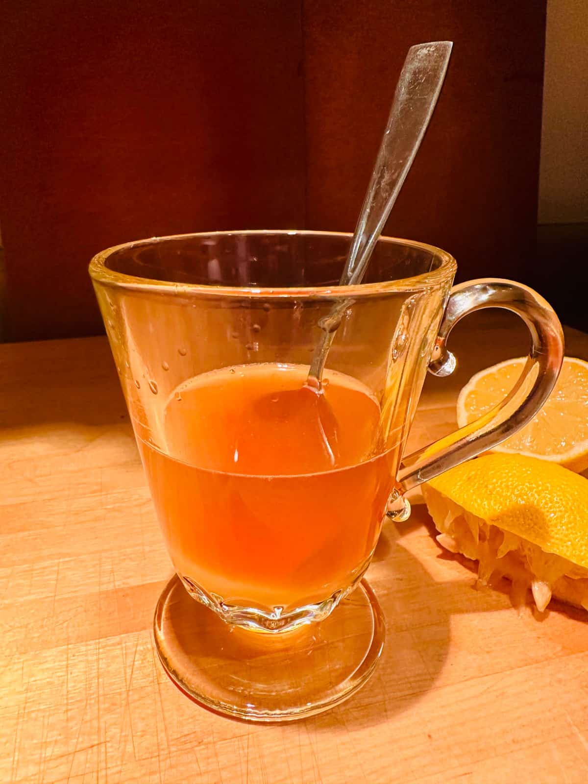 Glass mug containing finished whiskey hot toddy and a spoon.