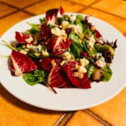 Red and green salad leaves sprinkled with blue cheese and nuts on a white plate.