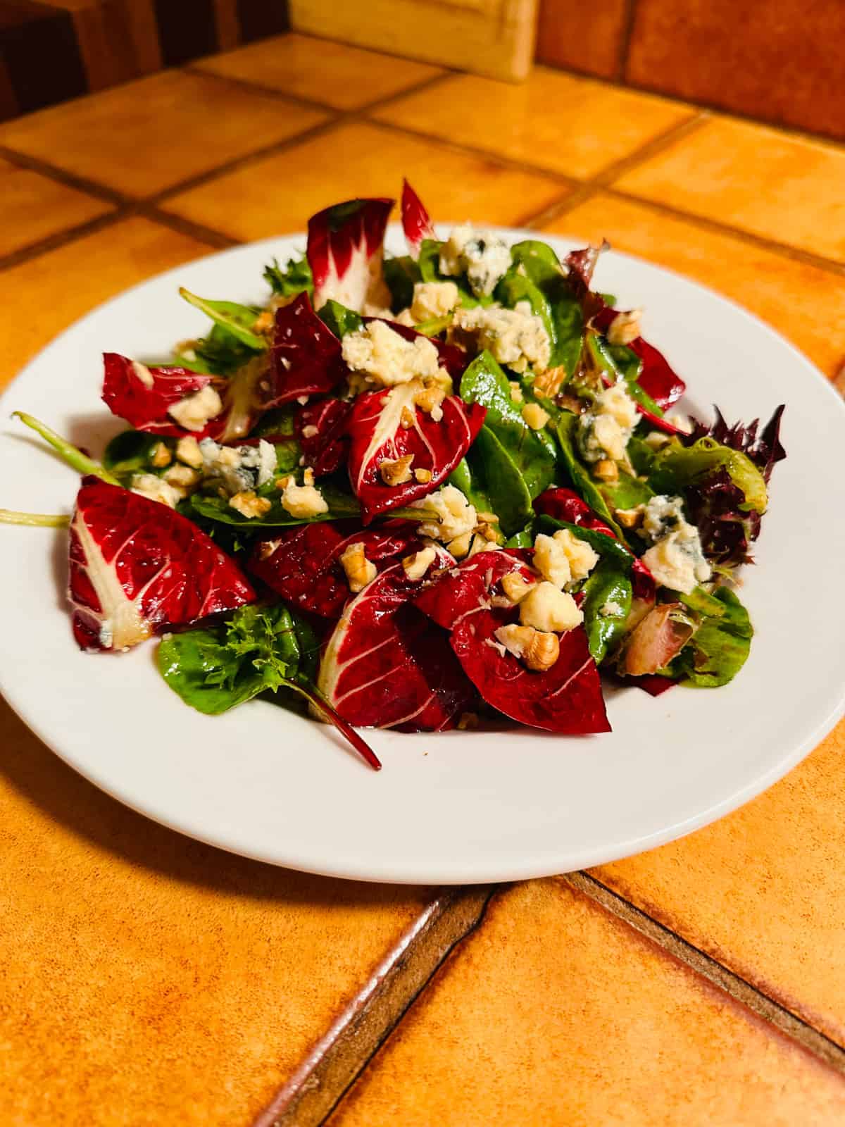 Red and green salad leaves sprinkled with blue cheese and nuts on a white plate.