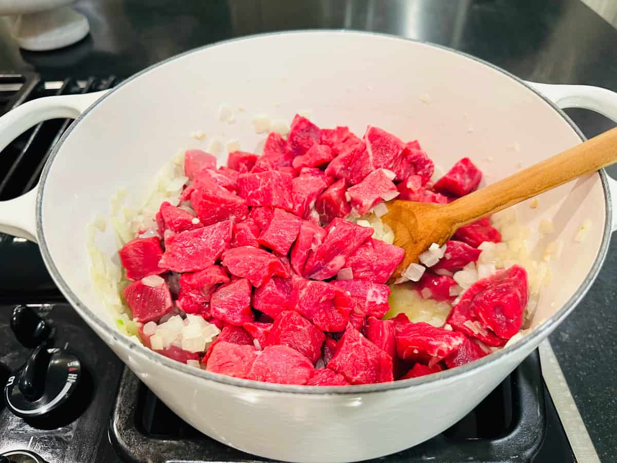 Raw meat in a white pot with a wooden spoon.