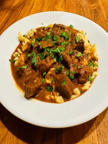 Goulash and spaetzle sprinkled with parsley on a white plate.