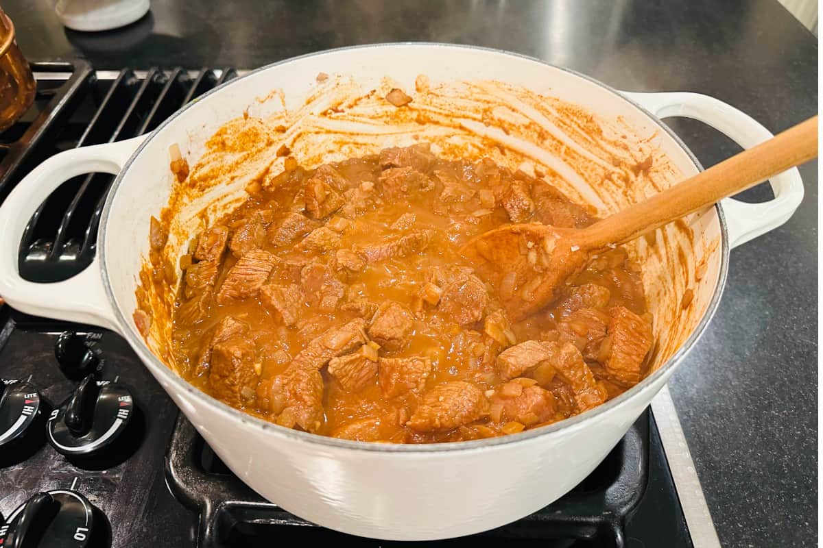Browned beef and onion mixture in a white pot with a wooden spoon.