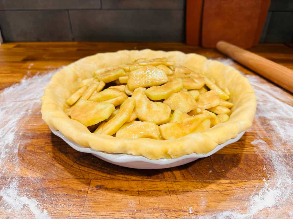 Sliced apples and unbaked pie dough in a white pie plate.